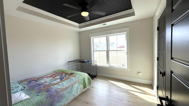 bedroom with light wood-style floors, a raised ceiling, and crown molding