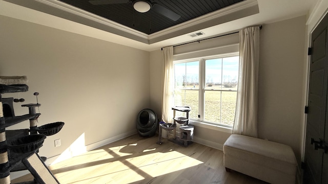 exercise area with light wood-style floors, visible vents, a raised ceiling, and crown molding