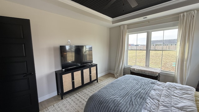 bedroom with a tray ceiling, light wood finished floors, visible vents, ornamental molding, and baseboards