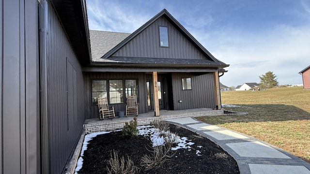 entrance to property with roof with shingles, a porch, a lawn, and board and batten siding