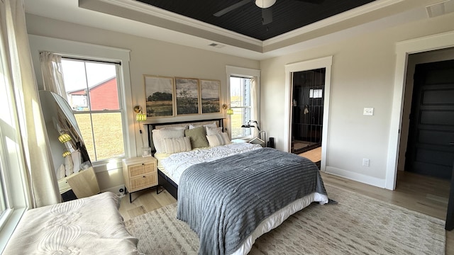 bedroom with a tray ceiling, visible vents, multiple windows, and wood finished floors