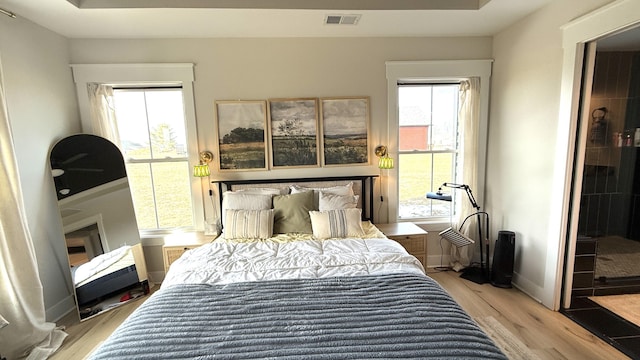 bedroom featuring light wood-style floors, multiple windows, visible vents, and baseboards