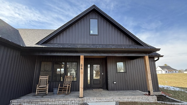 view of exterior entry with board and batten siding, covered porch, and roof with shingles