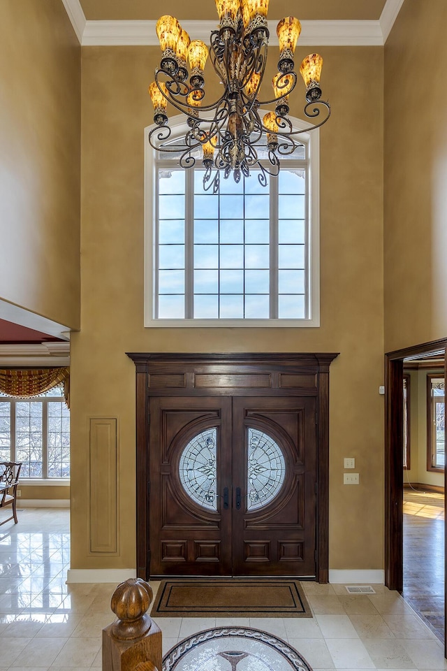 foyer entrance featuring baseboards, a high ceiling, visible vents, and crown molding