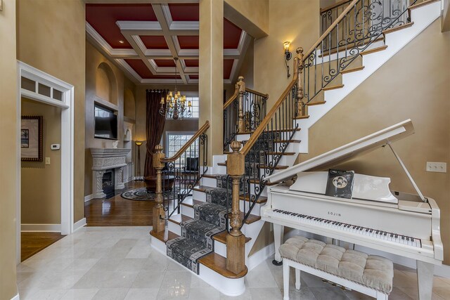 staircase with a chandelier, a high ceiling, coffered ceiling, and baseboards