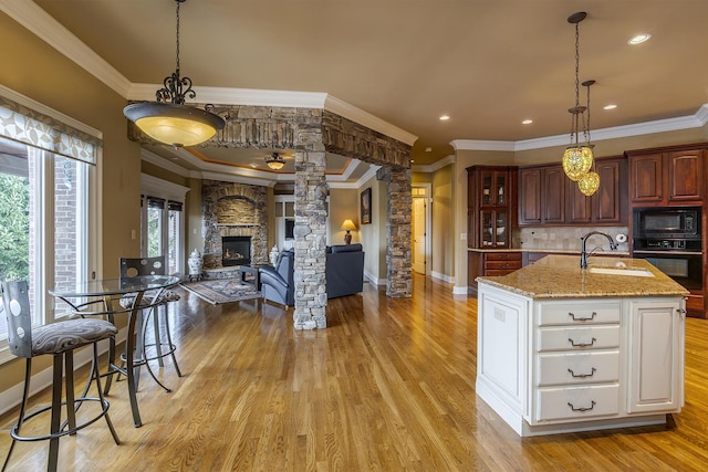 kitchen with ornate columns, light wood-type flooring, black appliances, a fireplace, and a sink