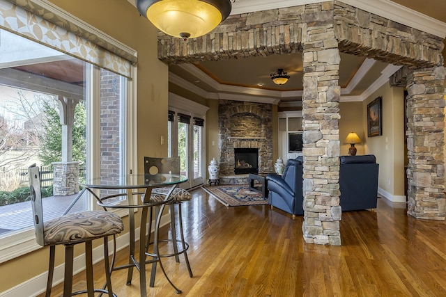 interior space featuring ornamental molding, a fireplace, decorative columns, and wood finished floors