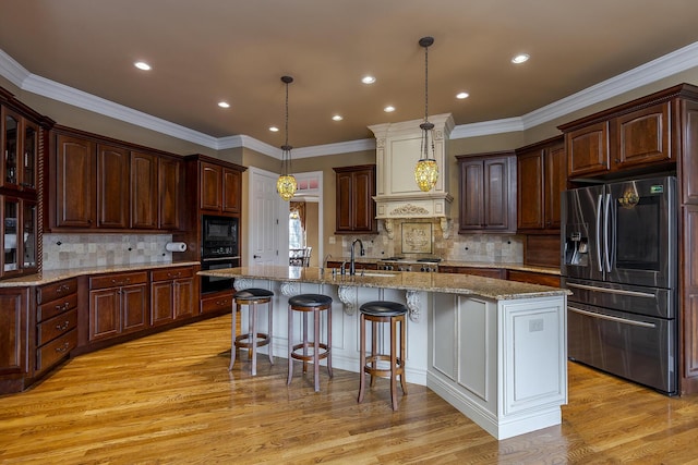 kitchen with a center island with sink, light wood-style flooring, a breakfast bar area, black appliances, and a sink