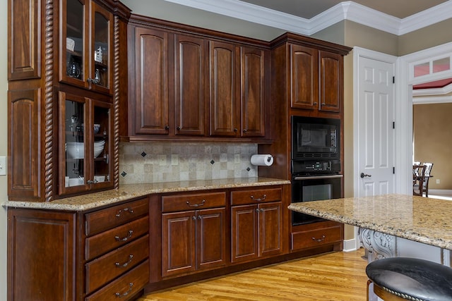 kitchen with light wood finished floors, light stone counters, glass insert cabinets, crown molding, and black appliances