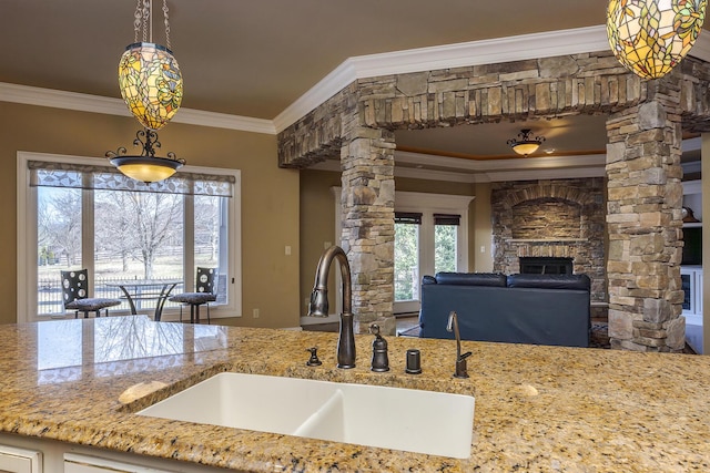 kitchen featuring decorative columns, ornamental molding, light stone counters, a fireplace, and a sink