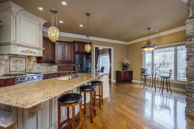 kitchen with light wood finished floors, decorative backsplash, high end range, black refrigerator with ice dispenser, and a sink