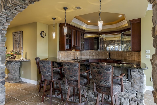 bar featuring hanging light fixtures, ornamental molding, a raised ceiling, and tasteful backsplash