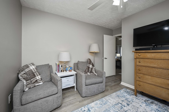 living area with a textured ceiling, ceiling fan, wood finished floors, and baseboards