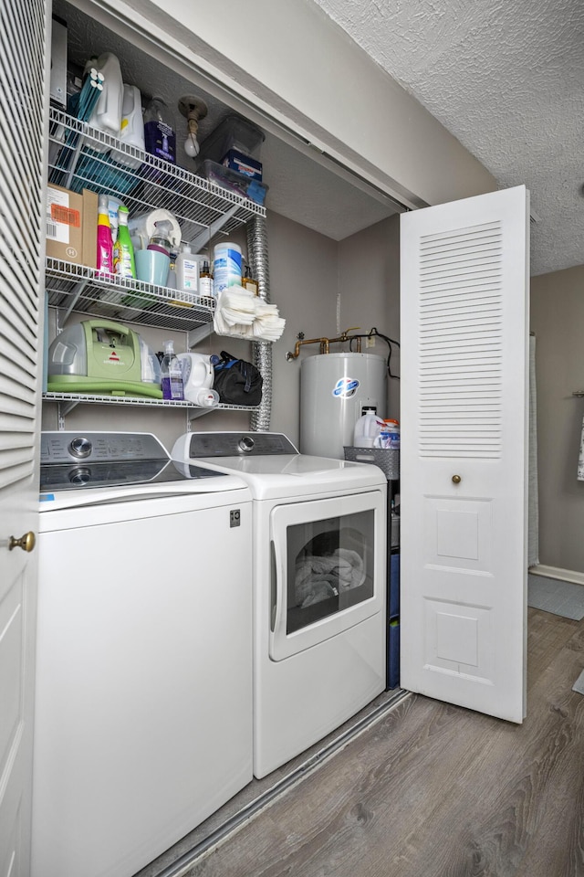 washroom with water heater, a textured ceiling, wood finished floors, washer and dryer, and laundry area