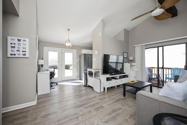 living area with ceiling fan with notable chandelier, light wood-type flooring, a wealth of natural light, and baseboards