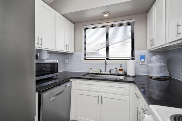 kitchen with stainless steel appliances, dark stone countertops, a sink, and white cabinets