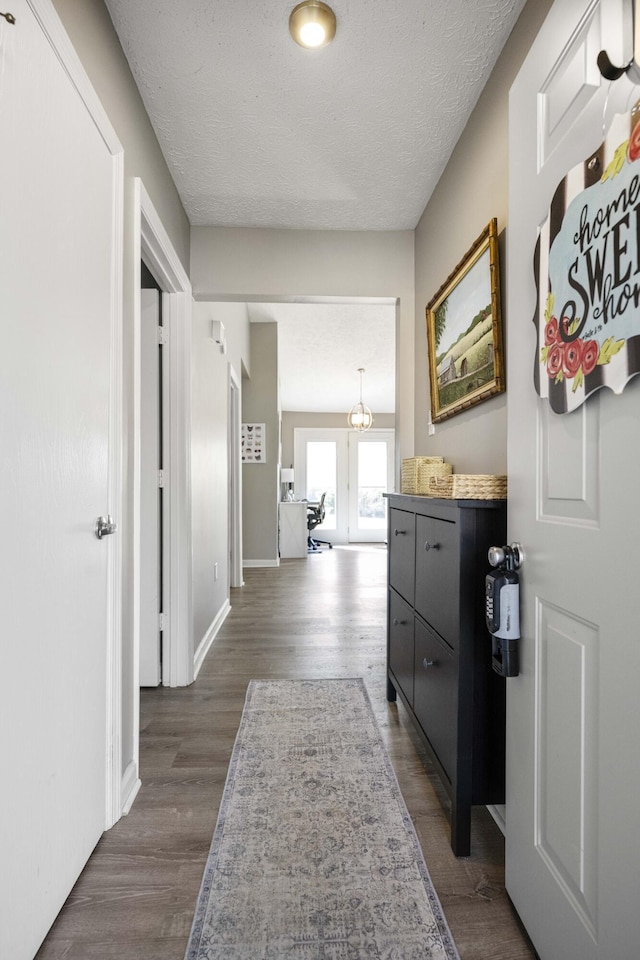 hall with a textured ceiling, dark wood finished floors, and baseboards