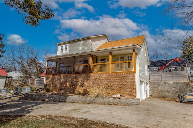 rear view of property with a garage, concrete driveway, central air condition unit, a porch, and brick siding