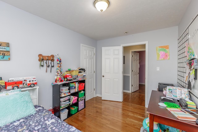 bedroom featuring baseboards, a textured ceiling, and light wood finished floors