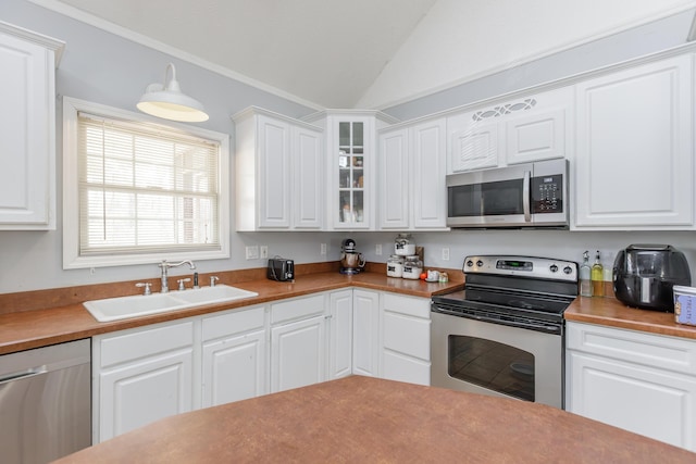 kitchen with appliances with stainless steel finishes, glass insert cabinets, a sink, and white cabinetry