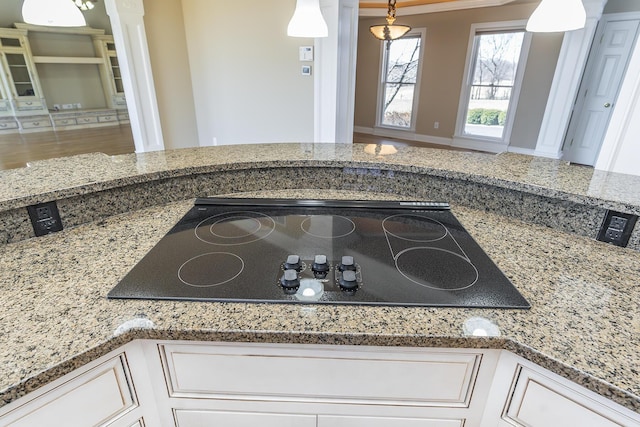 interior details featuring black electric stovetop, white cabinetry, light stone counters, and hanging light fixtures