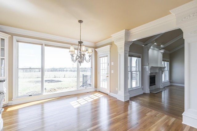 unfurnished dining area with decorative columns, crown molding, a notable chandelier, a fireplace, and wood finished floors