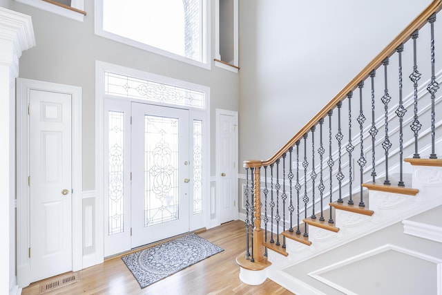 foyer with a high ceiling, visible vents, stairway, and wood finished floors