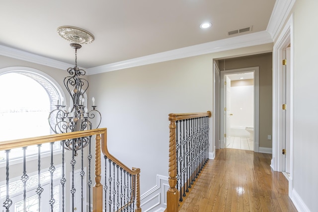 hallway with an upstairs landing, crown molding, a chandelier, light wood finished floors, and visible vents