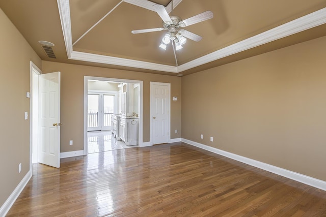 unfurnished room with a tray ceiling, baseboards, visible vents, a ceiling fan, and wood finished floors
