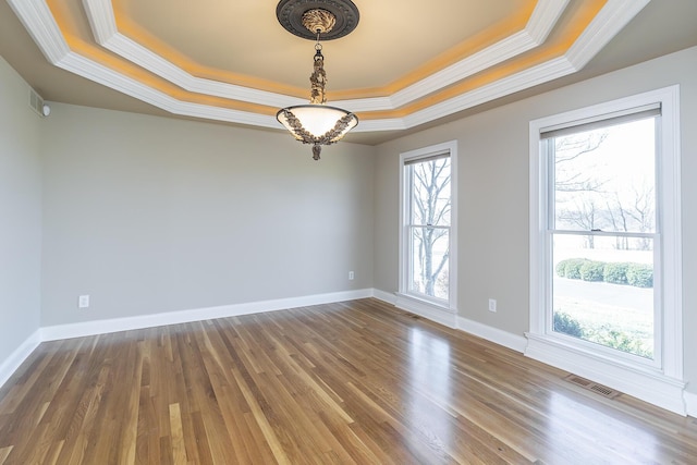spare room with a tray ceiling, visible vents, and wood finished floors
