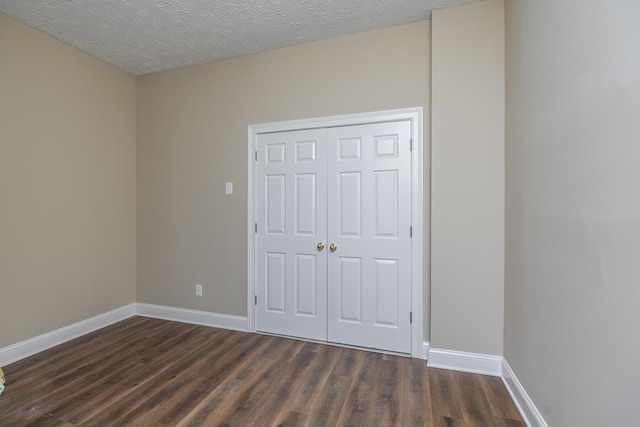 unfurnished bedroom with dark wood finished floors, baseboards, a closet, and a textured ceiling