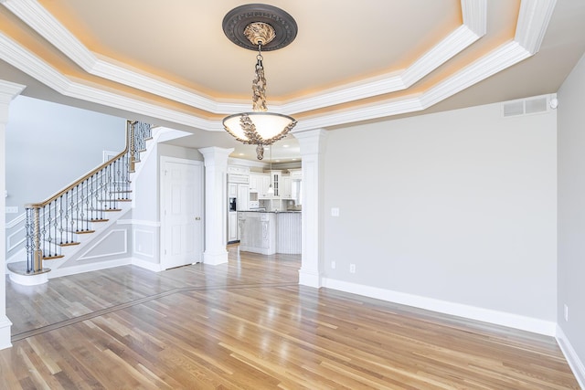 interior space featuring a tray ceiling, visible vents, light wood-style floors, and decorative columns