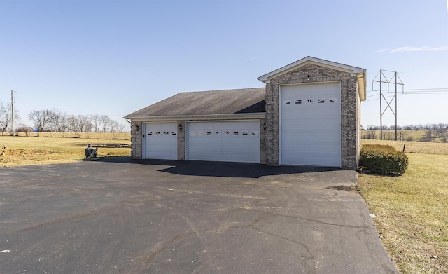 exterior space with a rural view, an outdoor structure, brick siding, and aphalt driveway