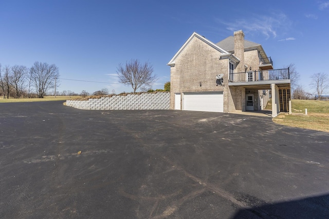 view of side of home with a chimney, stucco siding, a garage, and driveway