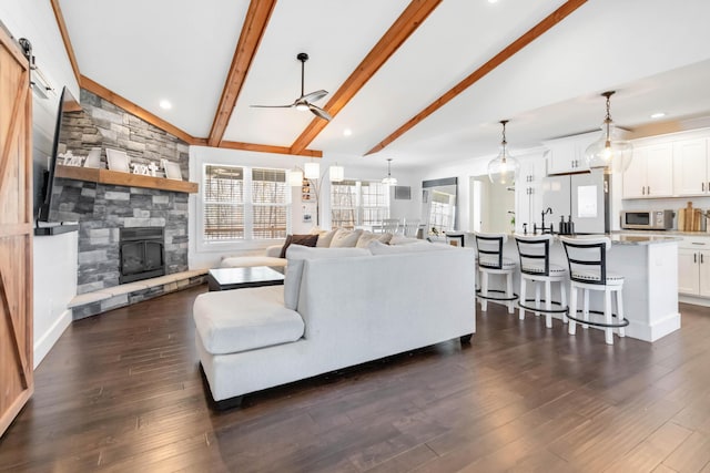 living room featuring a ceiling fan, dark wood-style flooring, vaulted ceiling with beams, a stone fireplace, and recessed lighting