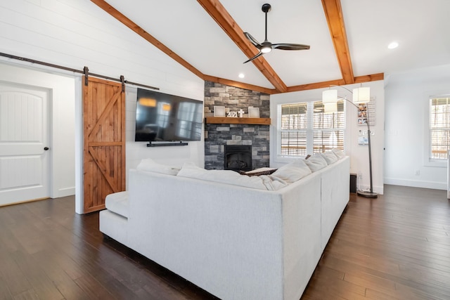 living room with lofted ceiling with beams, ceiling fan, a barn door, a stone fireplace, and dark wood finished floors