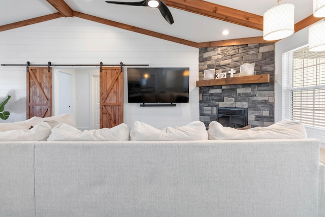 living room featuring vaulted ceiling with beams, a stone fireplace, a barn door, and a ceiling fan