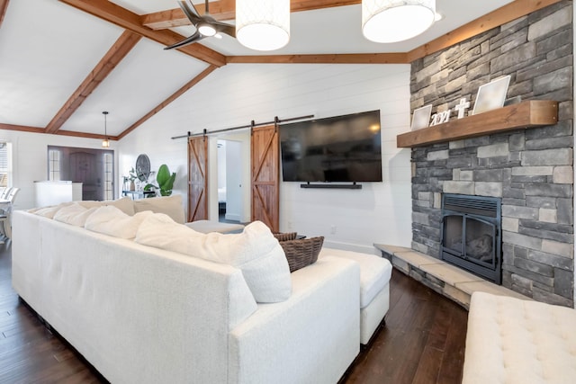 living room with lofted ceiling with beams, a barn door, dark wood-style flooring, and a stone fireplace