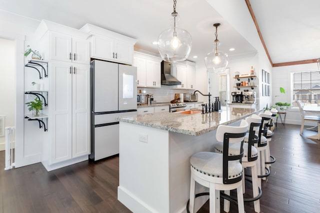 kitchen featuring freestanding refrigerator, white cabinetry, decorative light fixtures, and an island with sink