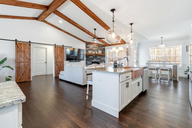 kitchen with a barn door, an island with sink, open floor plan, white cabinetry, and pendant lighting