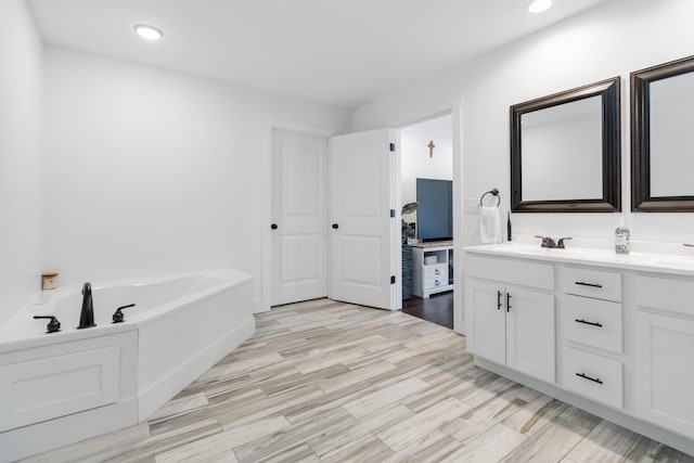 bathroom with a garden tub, recessed lighting, wood finished floors, and vanity