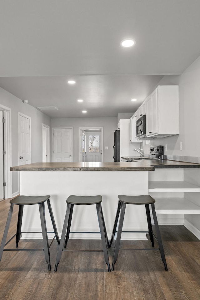 kitchen featuring black appliances, a breakfast bar, dark countertops, and white cabinets