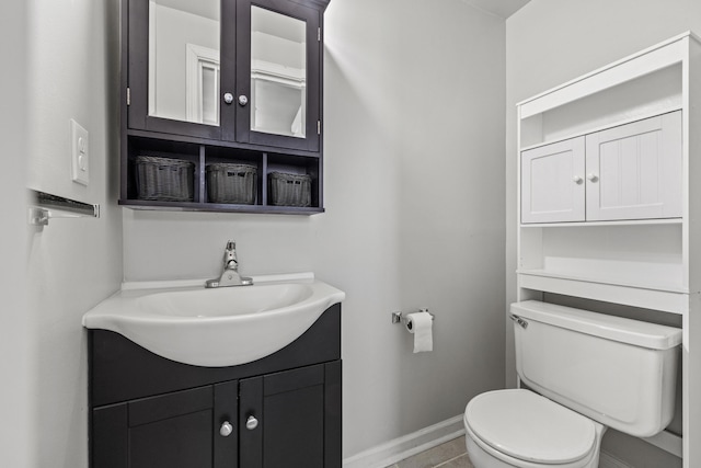 half bath featuring baseboards, vanity, and toilet