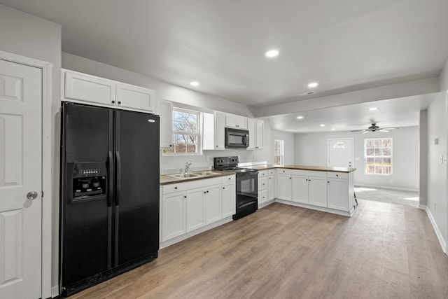 kitchen with open floor plan, white cabinets, a sink, a peninsula, and black appliances