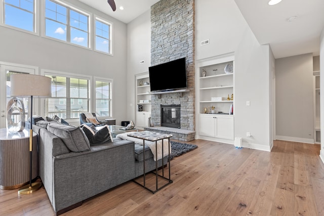 living room featuring a fireplace, a ceiling fan, baseboards, built in features, and light wood-style floors