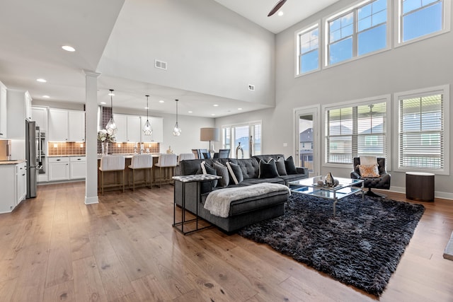 living area with light wood-style floors, a healthy amount of sunlight, decorative columns, and visible vents