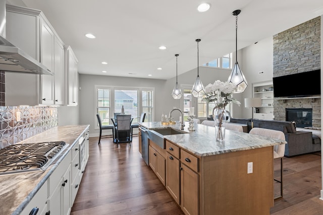 kitchen with open floor plan, white cabinetry, wall chimney range hood, and an island with sink