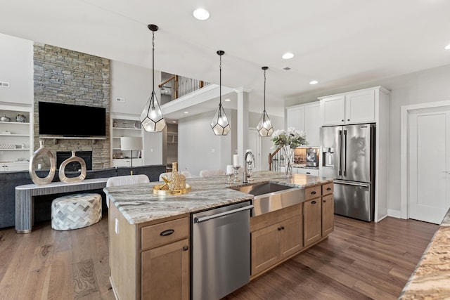 kitchen with white cabinets, appliances with stainless steel finishes, open floor plan, light stone countertops, and a sink