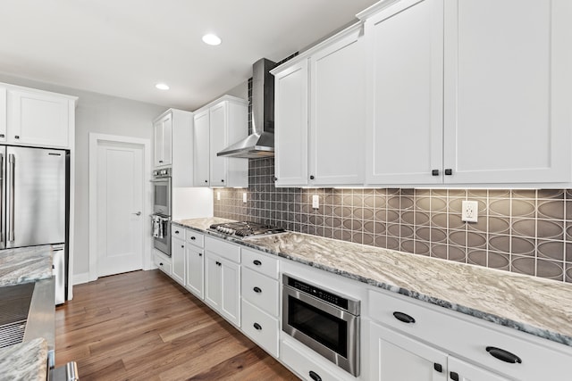 kitchen with light stone countertops, wall chimney range hood, white cabinetry, and appliances with stainless steel finishes