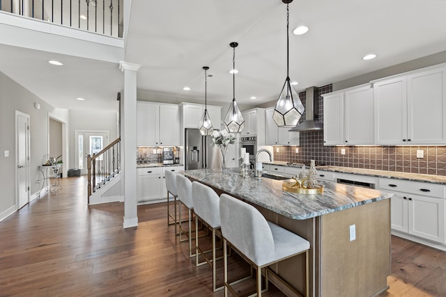 kitchen featuring a center island with sink, light stone counters, white cabinets, and decorative light fixtures